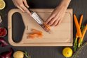 Chef snijdt zalm op houten plank met Tefal mes. Naast wortels, citroen, aardappel en ui.