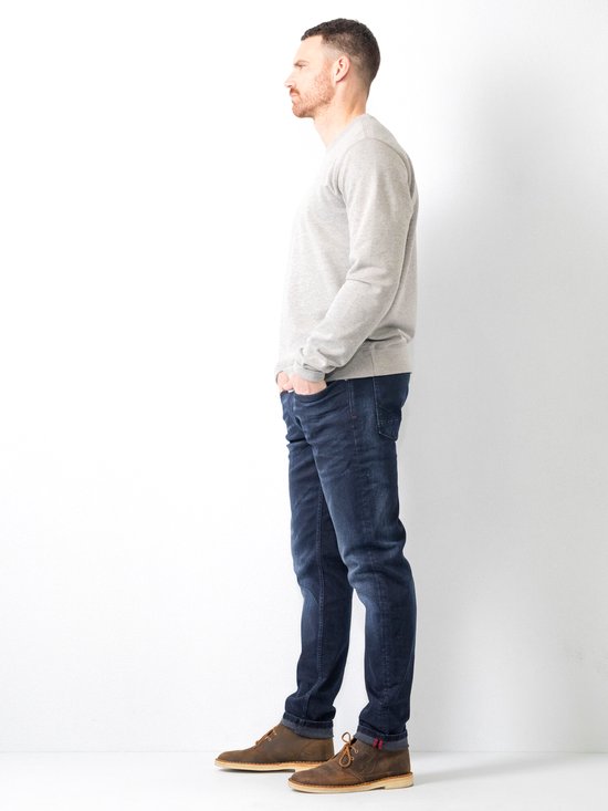 Man, profiel aanzicht, draagt een grijze trui en donkerblauwe jeans.
