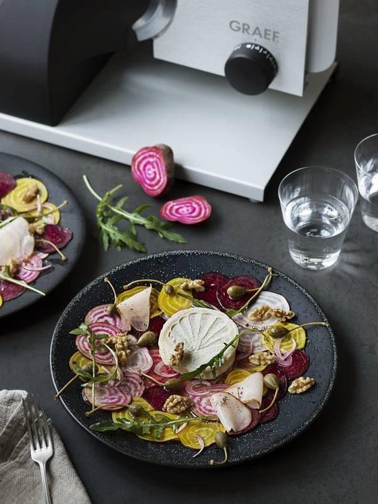Bovenaanzicht van een Graef snijmachine naast een bord met bietensalade en twee glazen water.