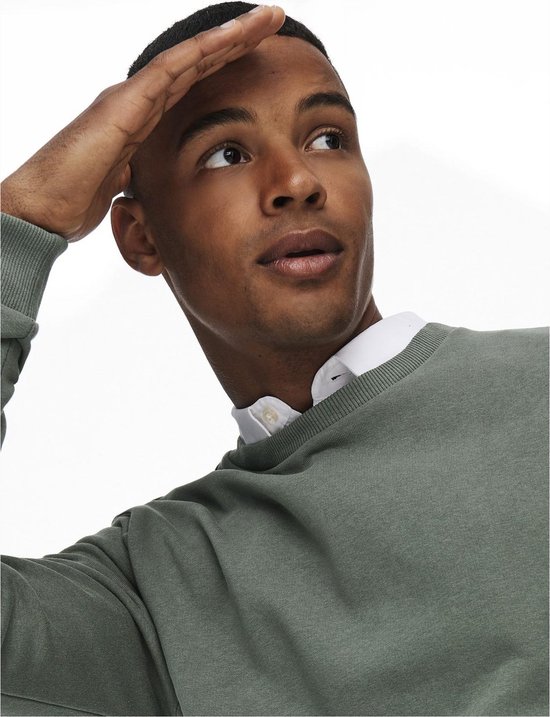 Man met gesloten ogen, kijkend naar rechts met hand op voorhoofd. Draagt een groene sweater met witte overhemdkraag.