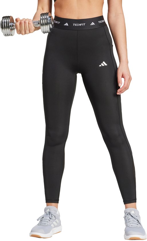 Vrouw in een zwarte Techfit legging met mesh-panelen en driestrepenlogo, die een dumbbell vasthoudt. Zittende pose.