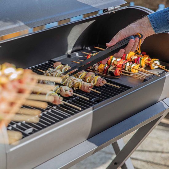 Hand met een Boretti tang die vleesspiesen op een BBQ draait.