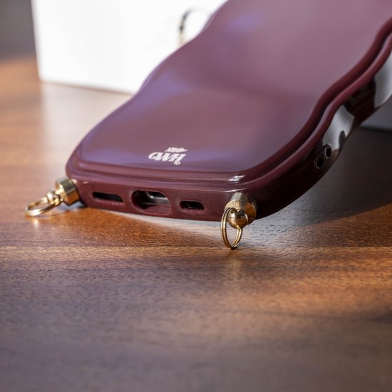 Detail van een glanzend bordeauxrood wavy telefoonhoesje voor iPhone 12 Pro Max met gouden oogjes.