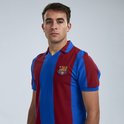 Jonge man met een FC Barcelona shirt met verticale blauwe en bordeauxrode banen, op een grijze achtergrond