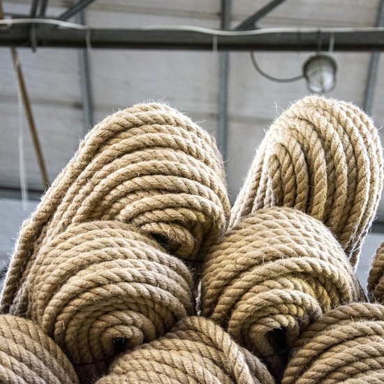 Pile de cordes en jute enroulées dans un entrepôt, avec des lumières visibles au plafond.