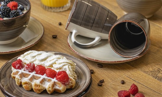 Grijze mokken en ontbijtborden met wafel, fruit en koffiebonen op houten tafel.