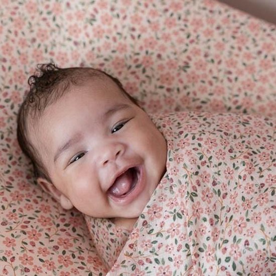 Lachende baby in een roze bloemenprint swaddle, omringd door roze bloemen.