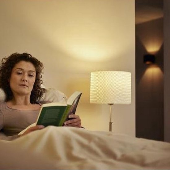 Vrouw leest boek in bed, naast een lamp met warme gloed.