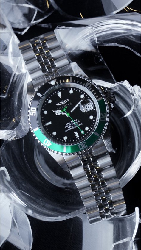 Herenhorloge met zwarte wijzerplaat, groene lunette, zilverkleurige band, tussen gebroken glas.