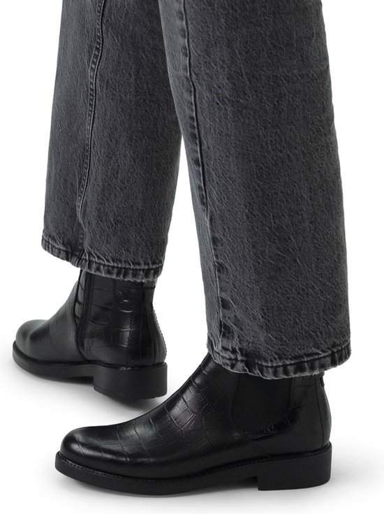Model draagt zwarte leren chelsea boots met crocoprint en jeans.