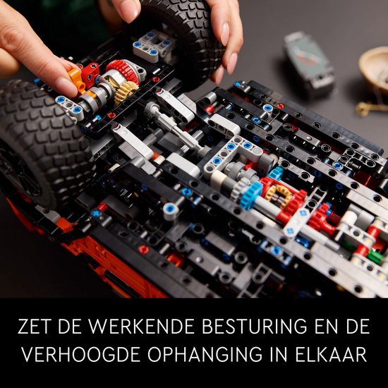 Onderkant van de oranje Mercedes-Benz G 500 modelauto, met zichtbare tandwielen en ophanging. "Zet de werkende besturing en de verhoogde ophanging in elkaar."