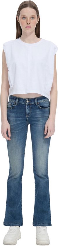Model draagt een flared spijkerbroek in donkerblauw met subtiele slijtageplekken. De broek is vanaf de knie wijd uitlopend.