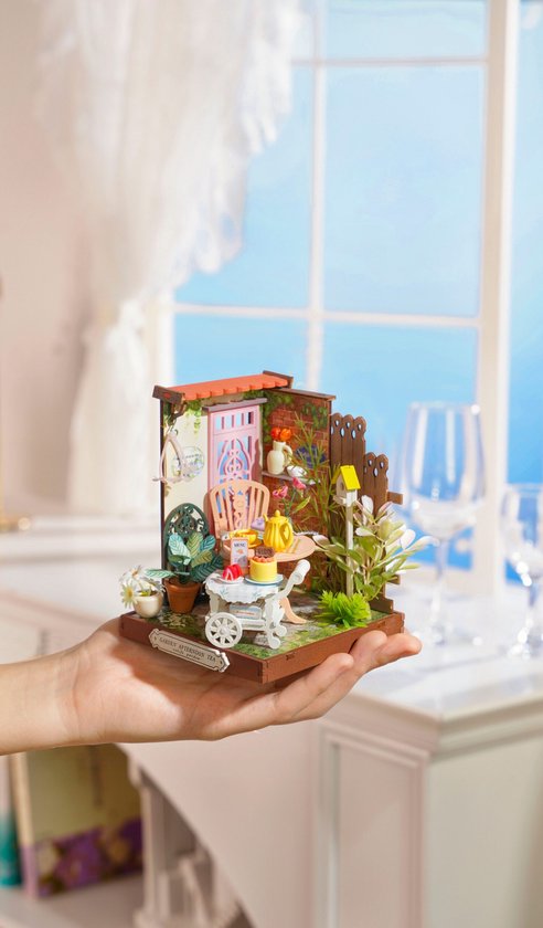 Een hand houdt een miniatuur 'Fancy Tea Yard' huisje vast.