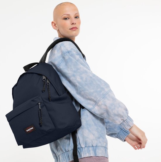 Vrouw met kort geschoren haar, met een lichtblauwe tie-dye jas, draagt een donkerblauwe Eastpak rugzak.