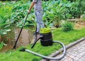 Man stofzuigt de rand van een vijver met een zwarte en groene vijverstofzuiger.