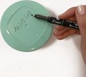 Hand met zwarte stift schrijft op een lichtgroen deksel.