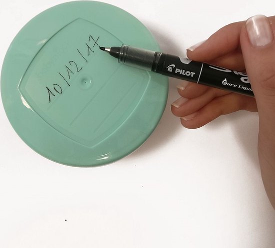 Hand met zwarte stift schrijft op een lichtgroen deksel.