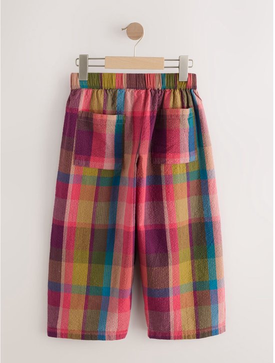 Geruite broek met wijde, ronde pijpen in rood, paars, groen en bruin.