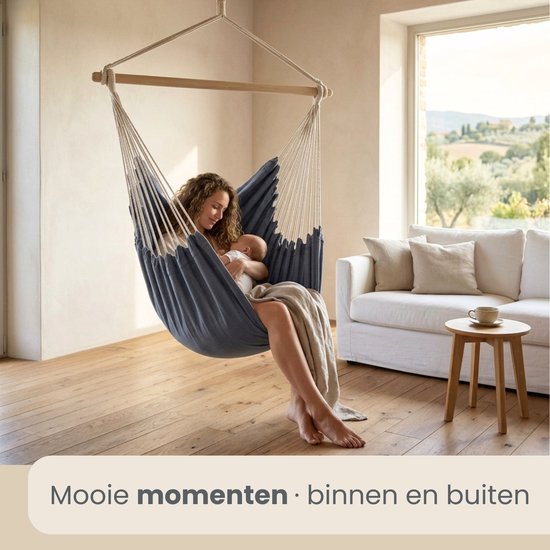 Vrouw met baby in een donkerblauwe hangmatstoel in een woonkamer.