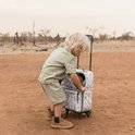 Jongetje met blond haar trekt een koffer met dierenprint in een safari-omgeving.