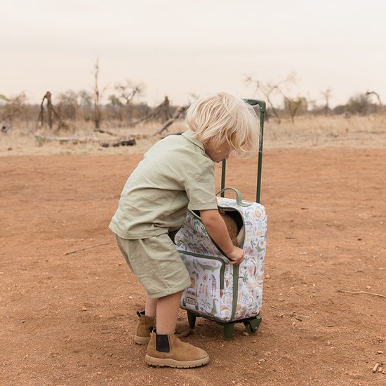 Jongetje met blond haar trekt een koffer met dierenprint in een safari-omgeving.
