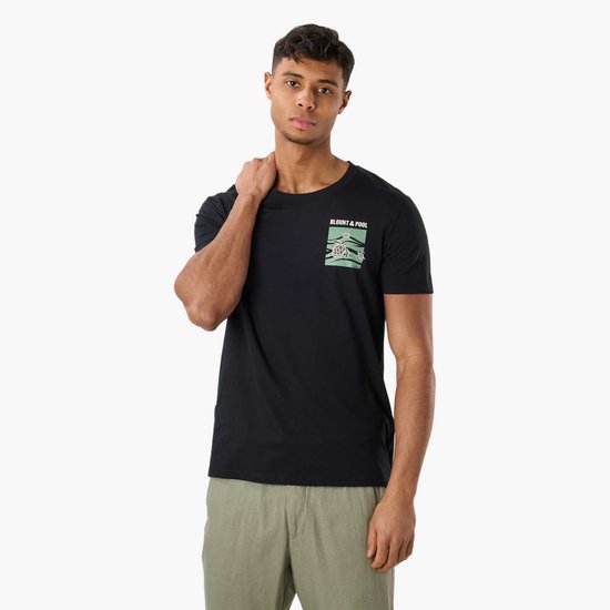 Man met zwarte t-shirt met schildpaddenprint op de borst, gekleed in groene broek.