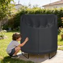 Zwarte trampolinehoes met rits in een achtertuin, een jongen raakt de hoes aan.
