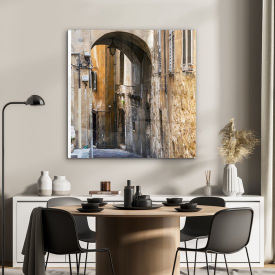 ® Glasschilderij 90x90 cm - Schilderij acrylglas - Stenen boog in een steegje tijdens een zonnige dag - Foto op glas - Muurdecoratie woonkamer - Wanddecoratie slaapkamer - Schilderijen