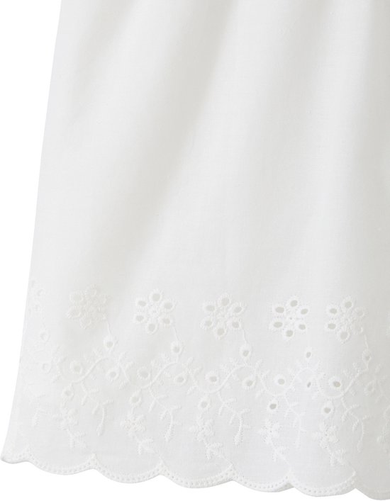 Detail van de zoom van een wit katoenen combishort met geborduurde bloemen en oogjes en een geschulpte rand.