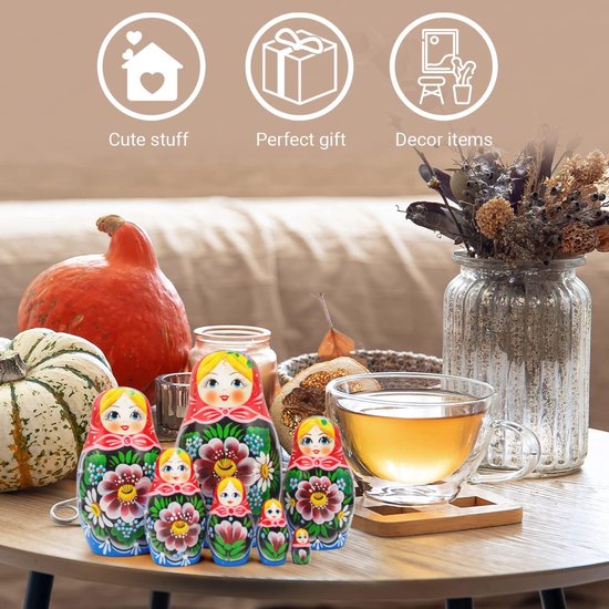 Zeven handgeschilderde Russische nestpoppen met bloemenpatronen, op een tafel met pompoenen en een kop thee.