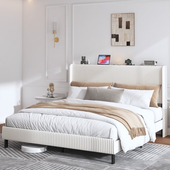 Lit rembourré de 180x200 cm en beige avec une tête de lit haute à canaux et des nervures horizontales. Le lit est décoré de coussins et d'une couverture.