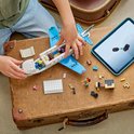 Jongen bouwt met tablet een wit en blauw LEGO vliegtuig op een bruine koffer.