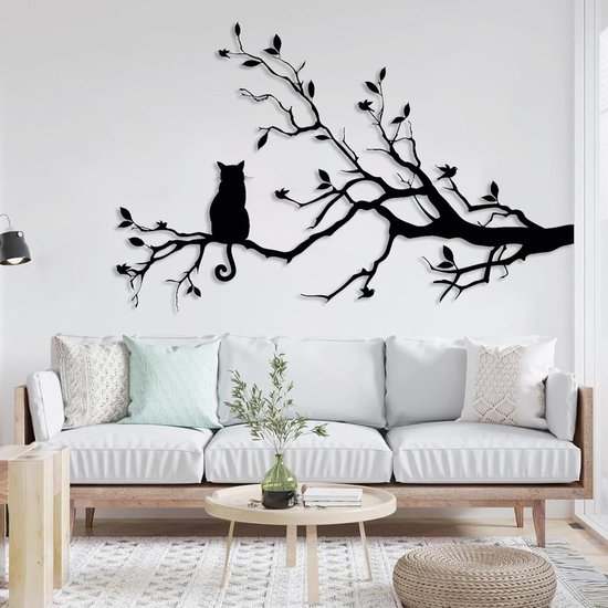 Chat noir en métal sur une branche avec des feuilles, au-dessus d'un canapé blanc.