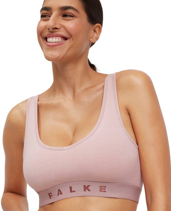 Une femme souriante aux cheveux bruns porte un soutien-gorge Falke rose avec une bande contrastante.