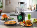 Zwarte Philips blender met een groene smoothie in de kan, met eten op het aanrecht.