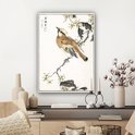 Une estampe japonaise avec un oiseau brun assis sur une branche aux fleurs jaunes, dans un cadre blanc au-dessus d'un buffet.