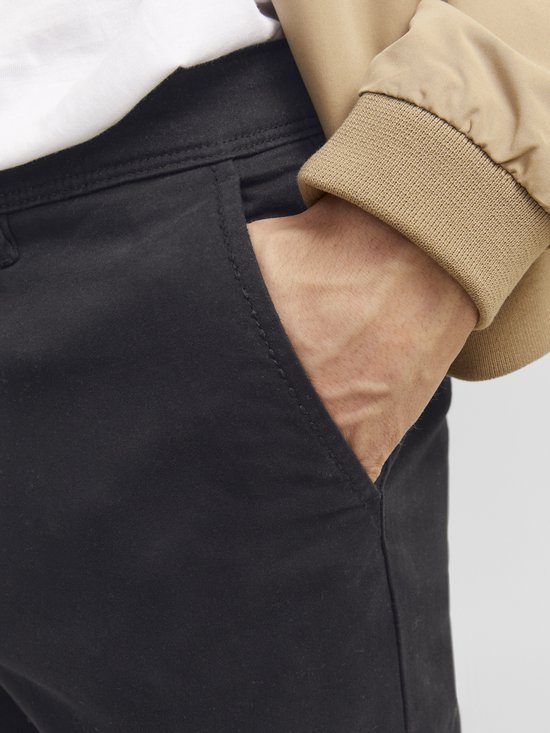 Detailopname van de zak van een zwarte chino met een beige bomberjack.