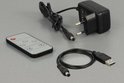 Zwarte afstandsbediening, stroomadapter met Europese stekker en USB-naar-DC-kabel op grijze achtergrond.