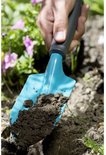 Een blauw tuinschepje met een grijs handvat dat aarde vasthoudt, in een bloembed.