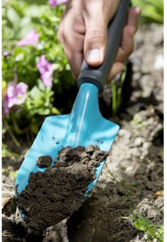 Een blauw tuinschepje met een grijs handvat dat aarde vasthoudt, in een bloembed.