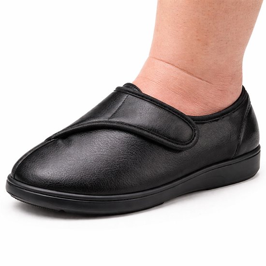 Zwarte, waterdichte, dames slipper met klittenbandsluiting, gedragen door een persoon.