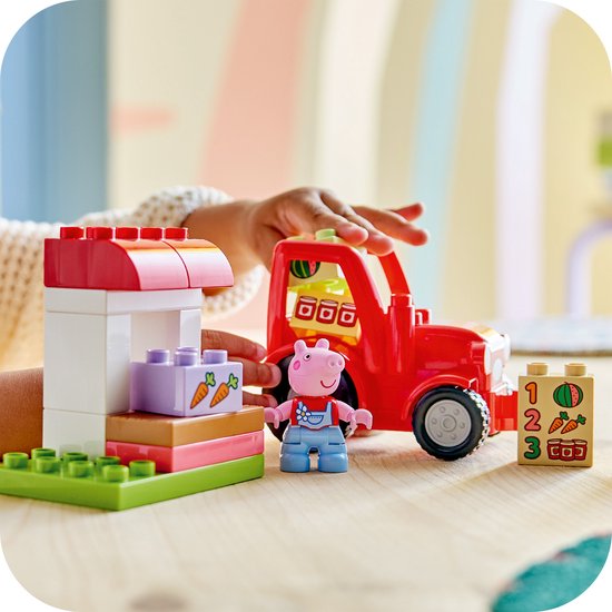 Kind speelt met LEGO Duplo Peppa Pig tractor, marktkraam, Peppa en nummerblok.
