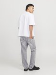 Man met korte, zwarte mullet, draagt een witte oversized top en lichtgrijze jeans. Zwart schoeisel.