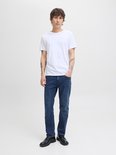 Jonge man met tatoeages, in een witte T-shirt en donkere jeans, hand in de zak.