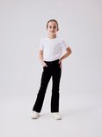 Meisje in een witte t-shirt en zwarte flared jeans, staat met handen in de zakken.