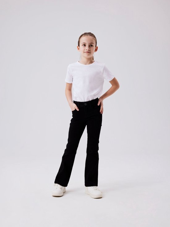 Meisje in een witte t-shirt en zwarte flared jeans, staat met handen in de zakken.