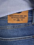 Close-up van het bruine leren label op de achterkant van een spijkerbroek, met 'DENIM DRIVEN SINCE 1989 CRAFTING QUALITY GARMENTS'.