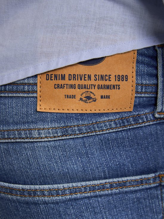 Close-up van het bruine leren label op de achterkant van een spijkerbroek, met 'DENIM DRIVEN SINCE 1989 CRAFTING QUALITY GARMENTS'.