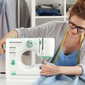 Vrouw met bril naait aan een blauwe stof op een witte Rynix naaimachine met groene details.