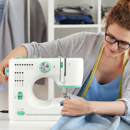 Vrouw met bril naait aan een blauwe stof op een witte Rynix naaimachine met groene details.
